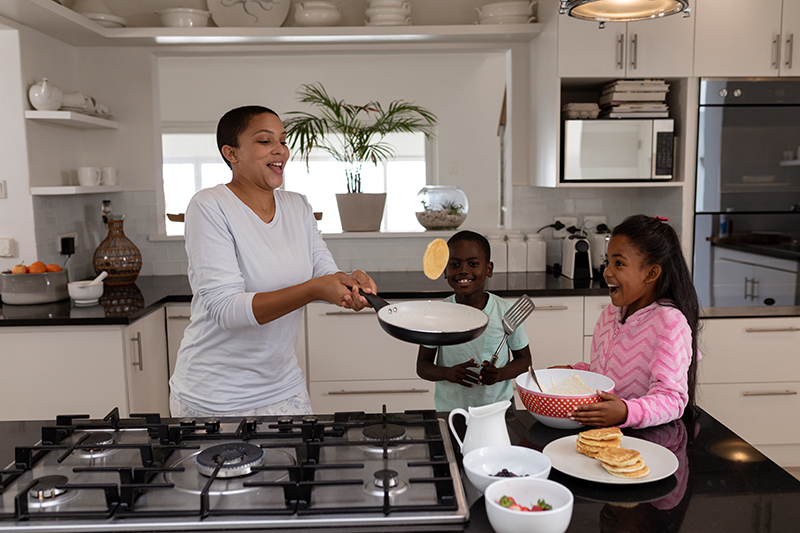 Mother And Children Preparing Food On A Worktop In Kitchen At Home